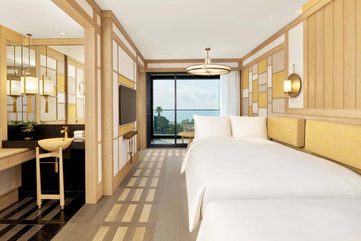 Habitación de hotel moderna con una cama grande, tocador con lavabo, televisión y vista al océano.