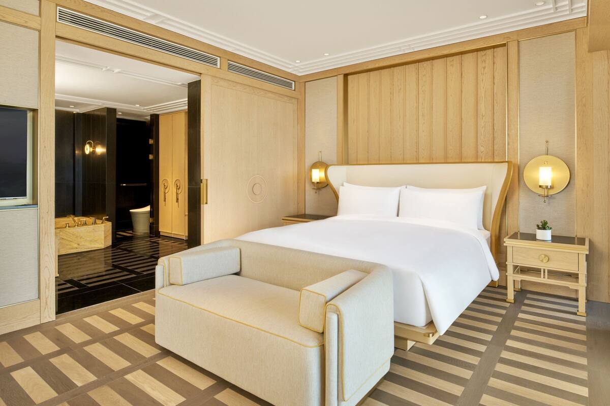 Una habitación de hotel moderna con una cama grande, un sofá, una mesita de noche y una lámpara de pared.