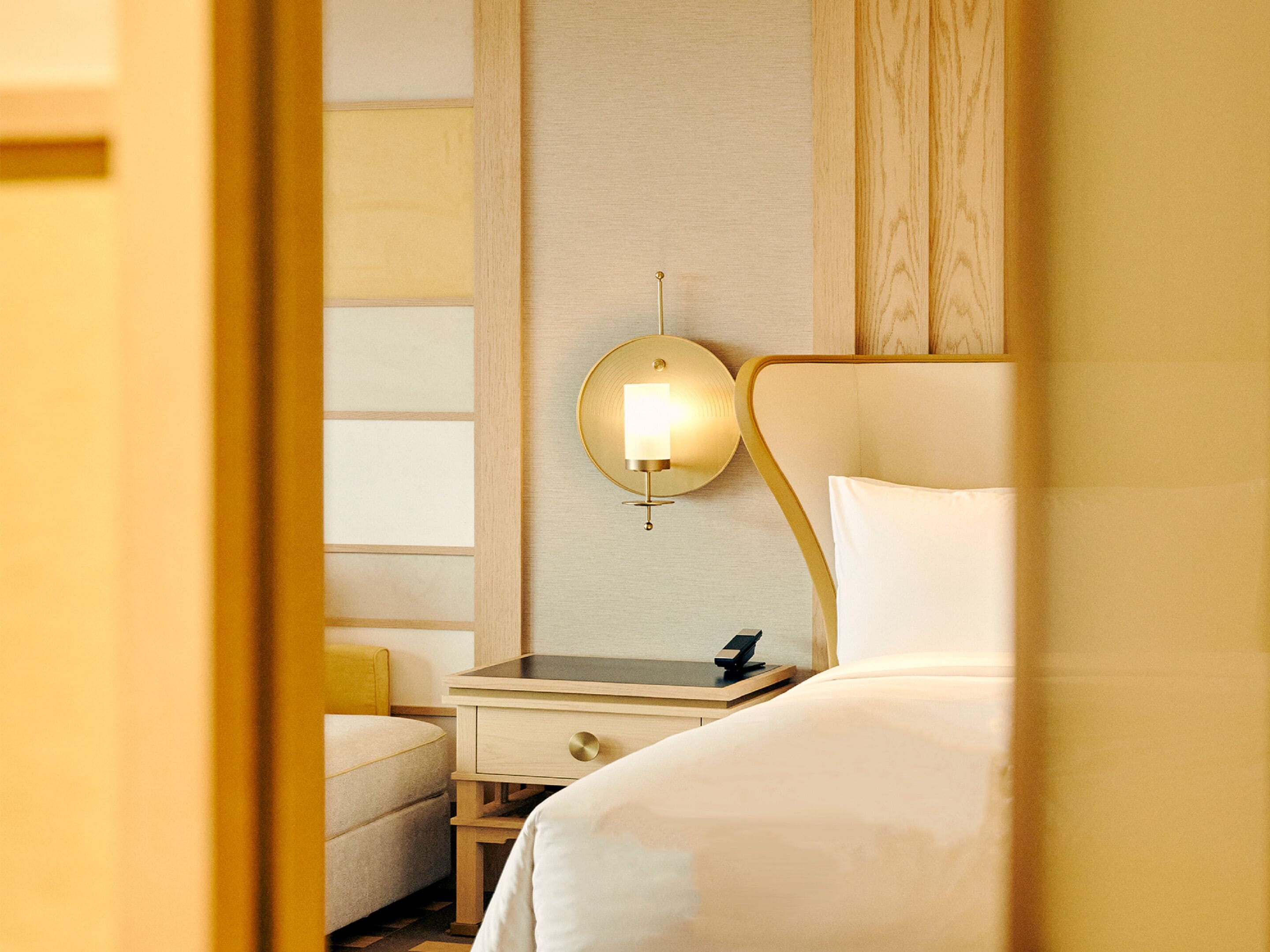 Una habitación de hotel con cama, mesita de noche y lámpara de pared.