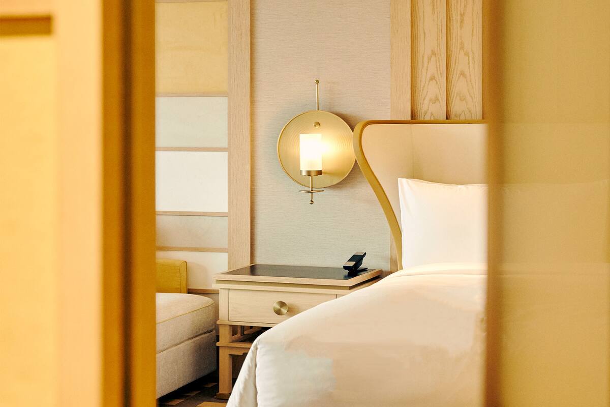 Una habitación de hotel con cama, mesita de noche y lámpara de pared.