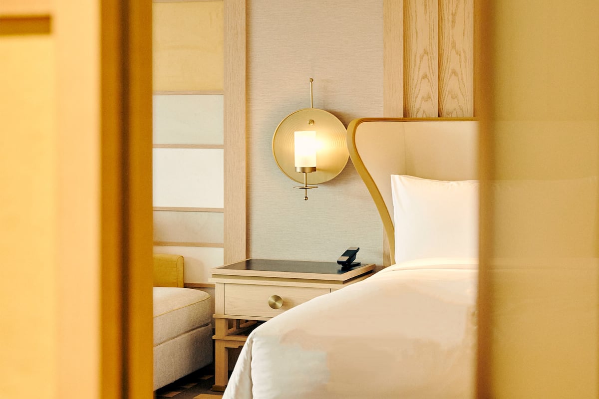 Una habitación de hotel con cama, mesita de noche y lámpara de pared.