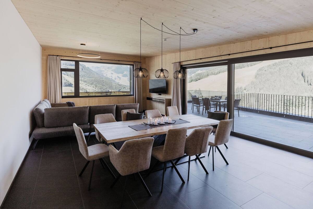 A modern dining area with a large table and chairs, a sofa, and a TV.