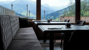 Ein Essbereich mit einer Bank und Tischen, großen Fenstern mit Blick auf die Berge und Kreuzen auf den Fensterbänken.