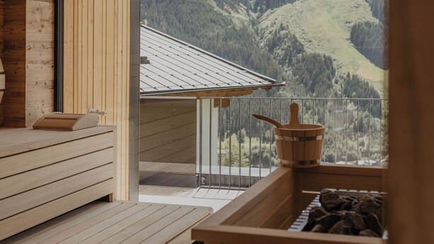 Eine Holzhütte mit Sauna, einer Holzbank und Blick auf eine Berglandschaft.