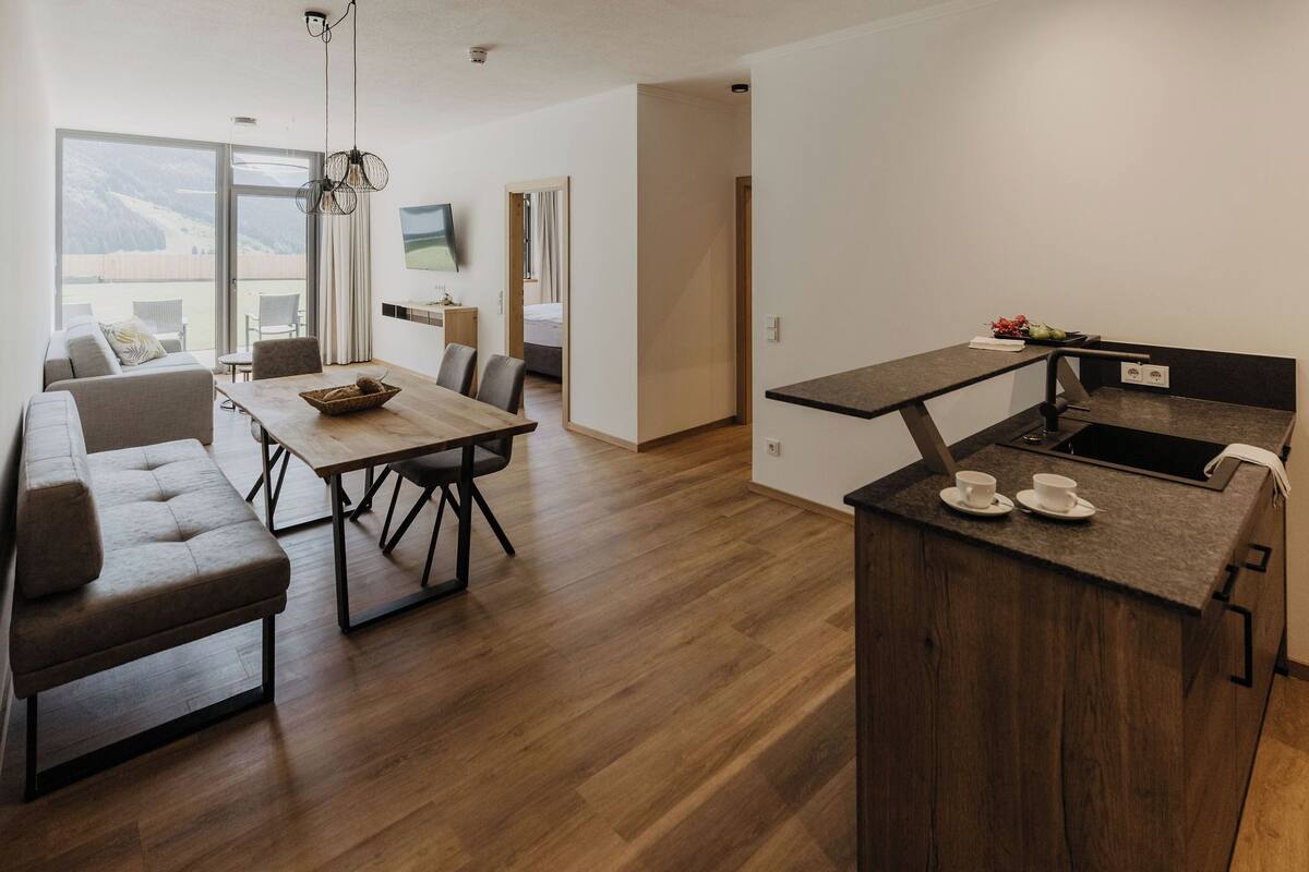 A modern kitchen with a wooden island, a dining area with a table and chairs, and a living area with a sofa and a TV.