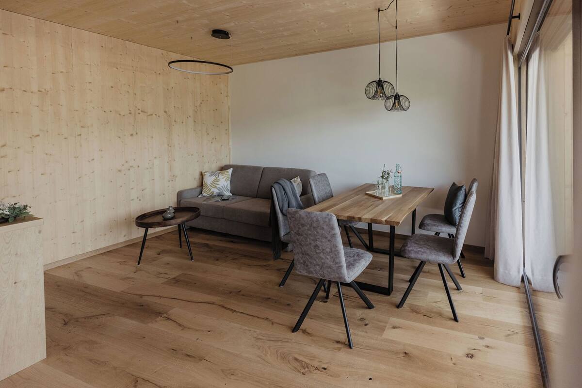 A modern dining area with a wooden table, grey upholstered chairs, and a grey sofa.