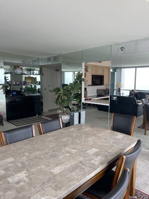 A modern living room with a dining area, kitchen, and a large mirror reflecting the space.
