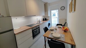 A modern kitchen with white cabinets, a built-in oven, and a dining area with a wooden table set for two. - S15 Studio Apartment Zagreb Croatia-free Parking (Zagreb)