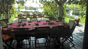 Un espace de restauration en plein air avec une table dressée pour six personnes, entourée de chaises, donnant sur une étendue d’eau.