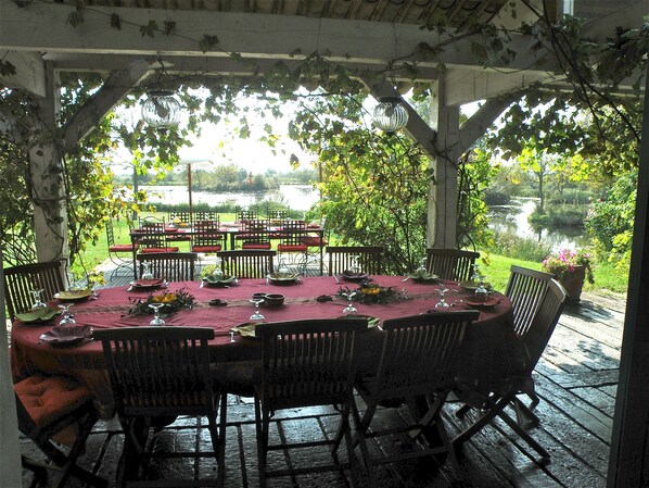 An outdoor dining area with a table set for six, surrounded by chairs, overlooking a body of water.