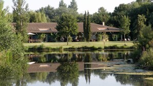Un cadre paisible au bord d’un lac, avec un bâtiment doté d’un toit en tuiles et d’une pelouse bien entretenue.