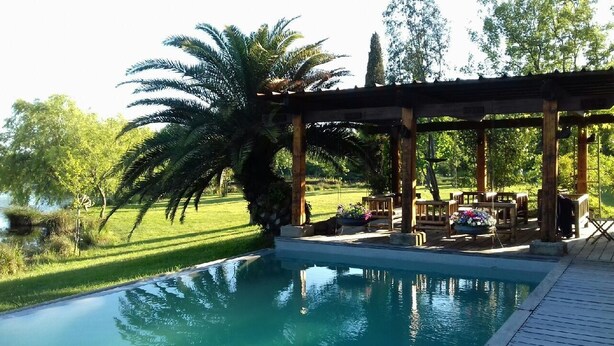 Un espace aménagé au bord de la piscine, avec une pergola, du mobilier d’extérieur et un palmier.