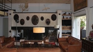 Un salon avec une cheminée, des canapés en cuir, une table basse et un grand tableau accroché au mur.