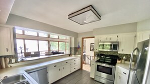 A modern kitchen with white cabinets, stainless steel appliances, and a large window providing natural light.