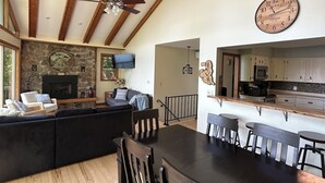 A spacious living area with a large wooden dining table, dark wooden chairs, and a stone fireplace.