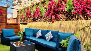 A blue sofa with cushions, a wicker coffee table, and a bamboo fence with hanging plants.