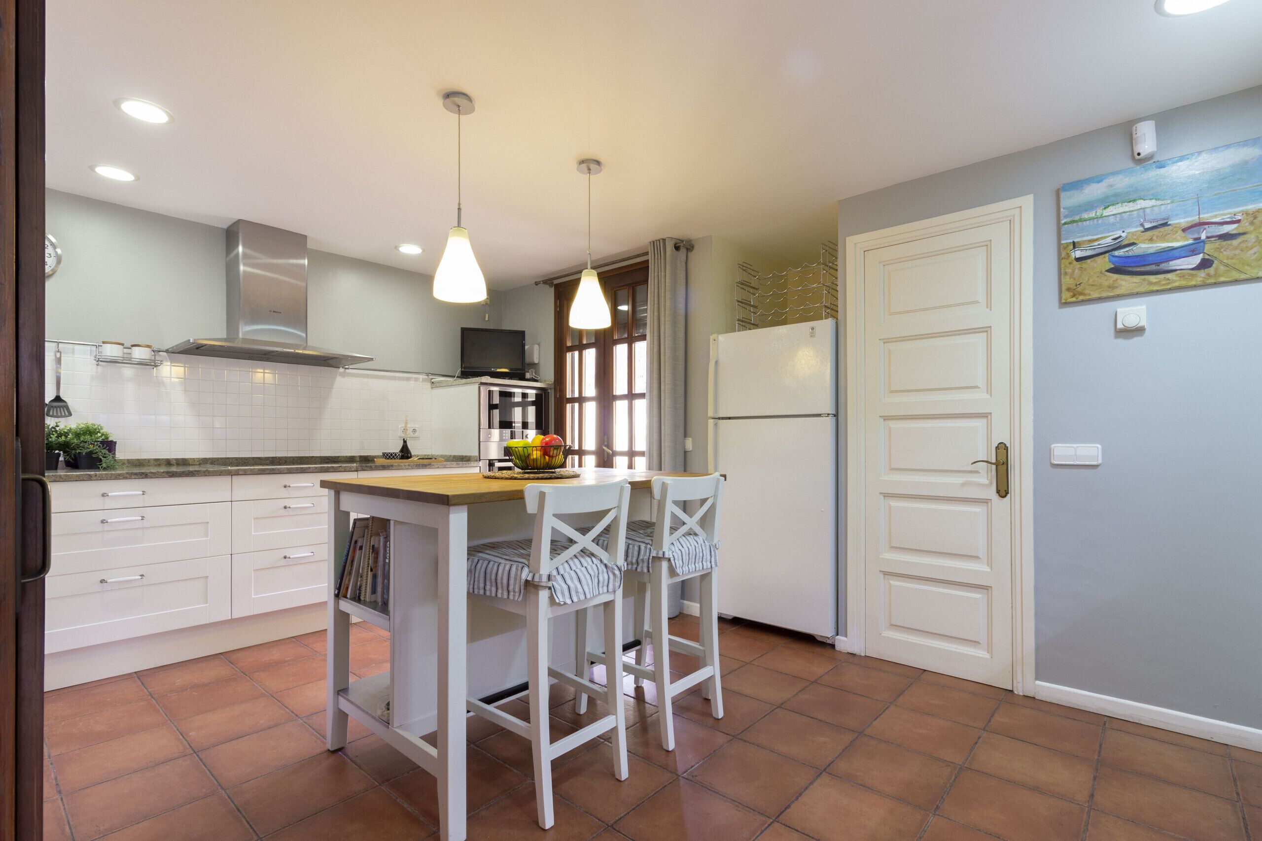 A kitchen with white cabinets, a central island, two chairs, a refrigerator, and a painting on the wall.