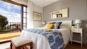 A bedroom with a bed, a bench, a nightstand, a mirror, and a balcony with a railing.
