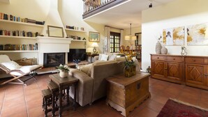 A spacious living room with a fireplace, bookshelves, a sofa, and a wooden cabinet.