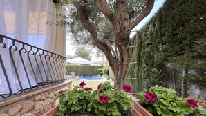 A stone wall, potted plants with flowers, a metal railing, and a tree.