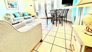 Een woonkamer met een bank, een eettafel met stoelen, een televisie en een plafondventilator.
