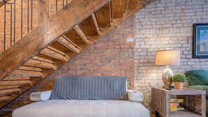 Un cuarto estilo loft con paredes de ladrillo visto, una escalera de madera, un sofá, una lámpara y una mesa pequeña con una planta.