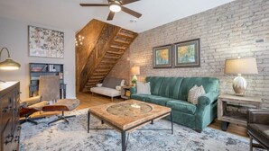 Una sala de estar acogedora con un sofá verde, una mesa de centro de madera y una escalera frente a una pared de ladrillo.