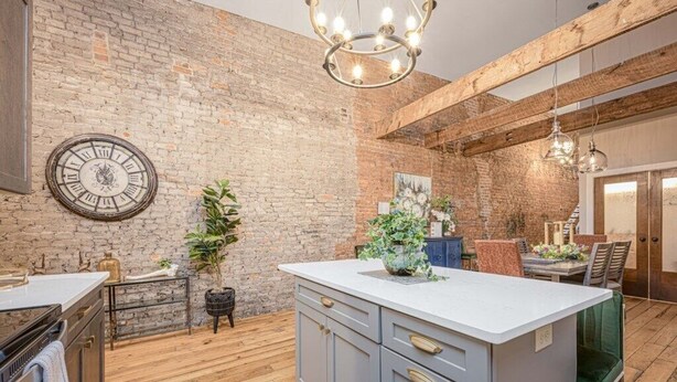 Una cocina con pared de ladrillo, suelo de madera, una isla central y una lámpara colgante.