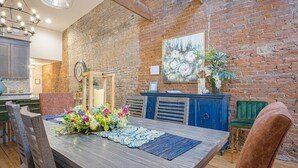 Un comedor con pared de ladrillo rústico, una mesa de madera con un centro de mesa floral y un armario azul.