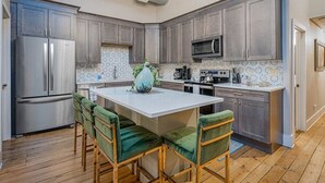 Una cocina moderna con gabinetes grises, electrodomésticos de acero inoxidable y una isla central con sillas tapizadas en verde.