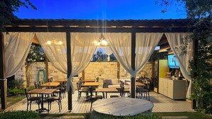 An outdoor patio with tables and chairs, a stone wall, and a TV screen. - Alaçatı Viola Hotel (Çesme)