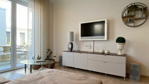 Una sala de estar moderna con un televisor de pantalla plana grande montado en la pared, una mesa de centro de vidrio, un sofá color beige y una mesita auxiliar con adornos.