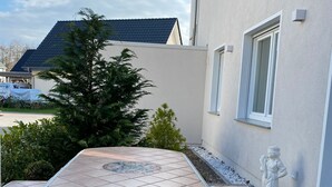 Un patio con una mesa y sillas de cerámica, rodeado por un muro bajo y una estatua.