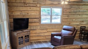 Un salon chaleureux avec un mur en bois, un téléviseur posé sur un meuble en bois, un canapé en cuir marron et un ventilateur de plafond.