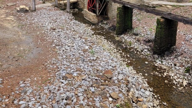 Une maison rustique en bois, dotée d’une roue à eau, entourée d’une forêt.