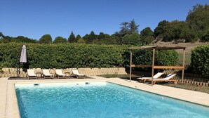 A rectangular swimming pool with clear blue water, surrounded by beige tiles. There are white lounge chairs and a pergola structure with a wooden roof. - New! Renovated cottage in old mill with swimming pool (Forcalquier)