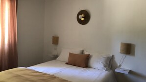 A neatly made bed with a beige blanket, two pillows, and a small wall-mounted lamp. - New! Renovated cottage in old mill with swimming pool (Forcalquier)