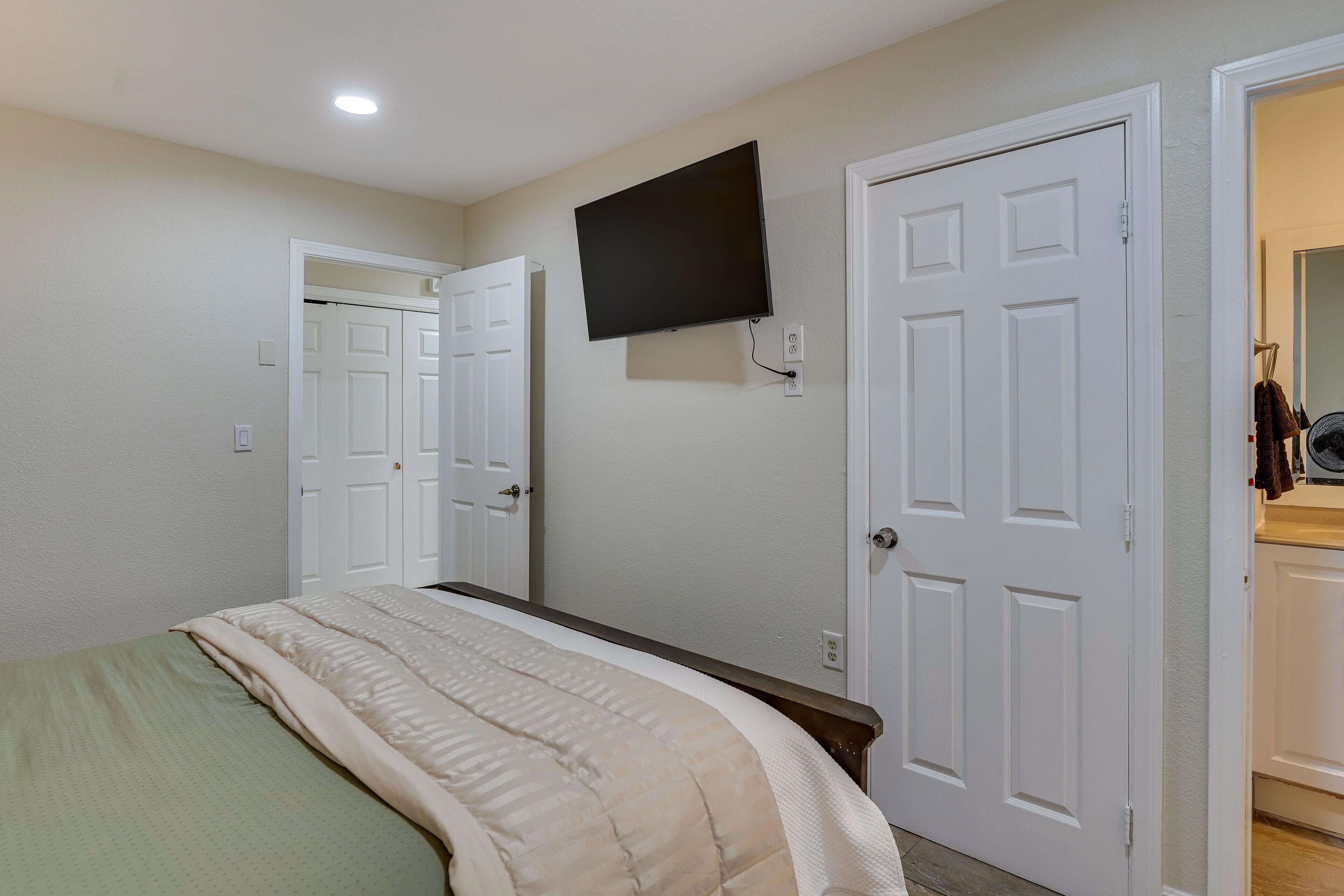 A bedroom with a bed, a television mounted on the wall, and two white doors.