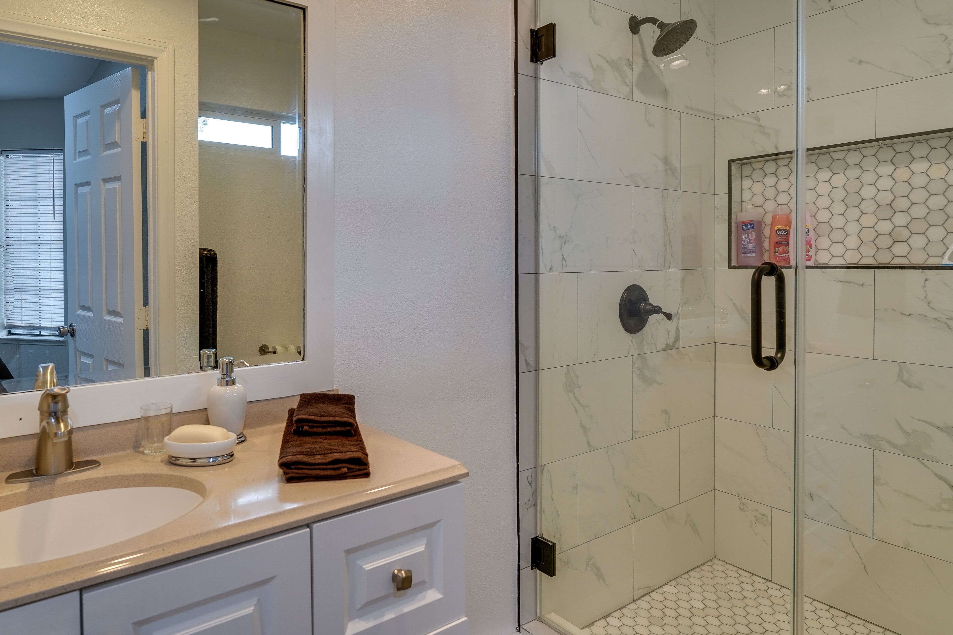 A bathroom with a white sink, a mirror, a glass shower enclosure, and a towel on the counter.