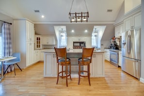 A spacious kitchen with white cabinetry, a central island with stools, stainless steel appliances, and pendant lighting.