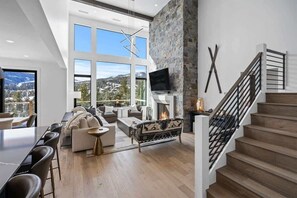 A spacious living room with a fireplace, a large window, and a staircase.