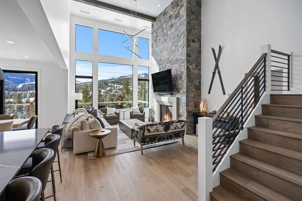 A spacious living room with a fireplace, a large window, and a staircase.