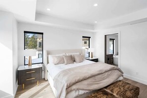 A modern bedroom with a large bed, bedside tables, a mirror, and a window with a view of the outside.