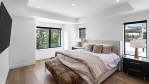 Un dormitorio moderno con una cama grande, suelo de madera y ventanas amplias que ofrecen vistas a un paisaje nevado.