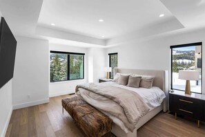 A modern bedroom with a large bed, wooden flooring, and large windows offering a view of a snowy landscape. - Breathtaking 5-Bed Mountain Modern Home (Big Sky)