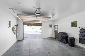 A garage with a large open door, a ceiling-mounted projector, and a covered grill.