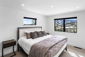 A bedroom with a bed, two nightstands, and two windows offering a mountain view.