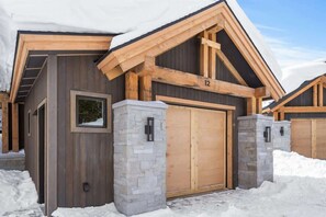 A modern log cabin with a stone foundation, wooden exterior, and a large garage door. - Breathtaking 5-Bed Mountain Modern Home (Big Sky)