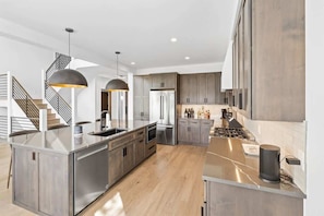 A modern kitchen with a central island, stainless steel appliances, and a staircase with a unique design.