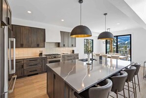 A modern kitchen with dark wood cabinets, a large island with bar stools, and pendant lighting.